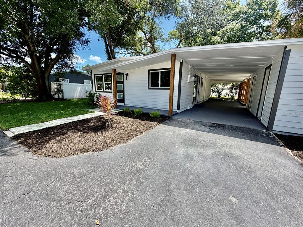 A white single-story house features a carport, a paved driveway, and a small landscaped yard — 7117 15TH STREET N, ST PETERSBURG, FL