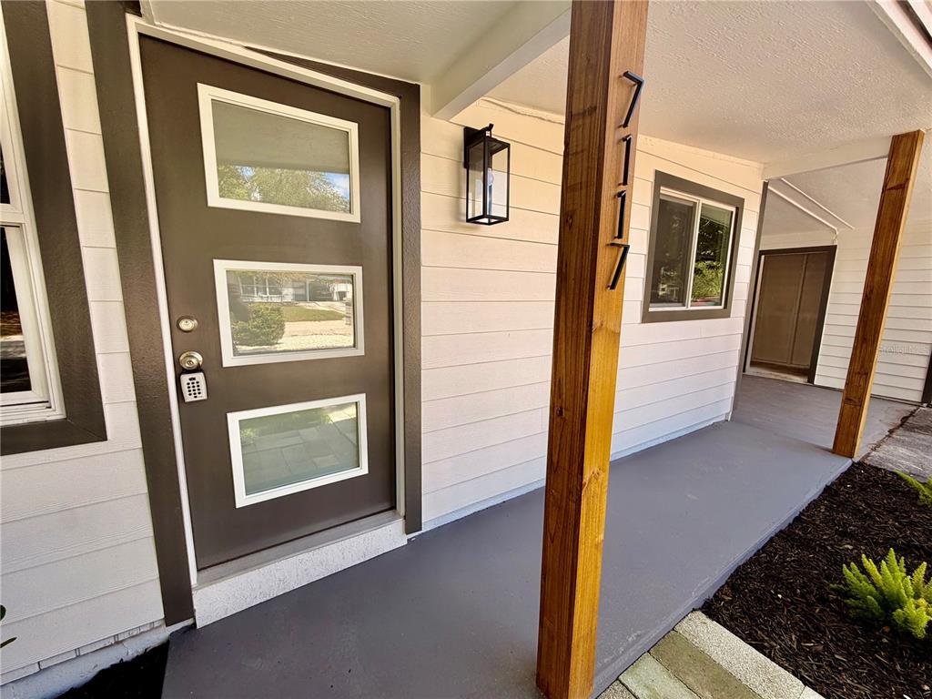 A brown front door with three windows sits next to a wooden post with house numbers — 7117 15TH STREET N, ST PETERSBURG, FL
