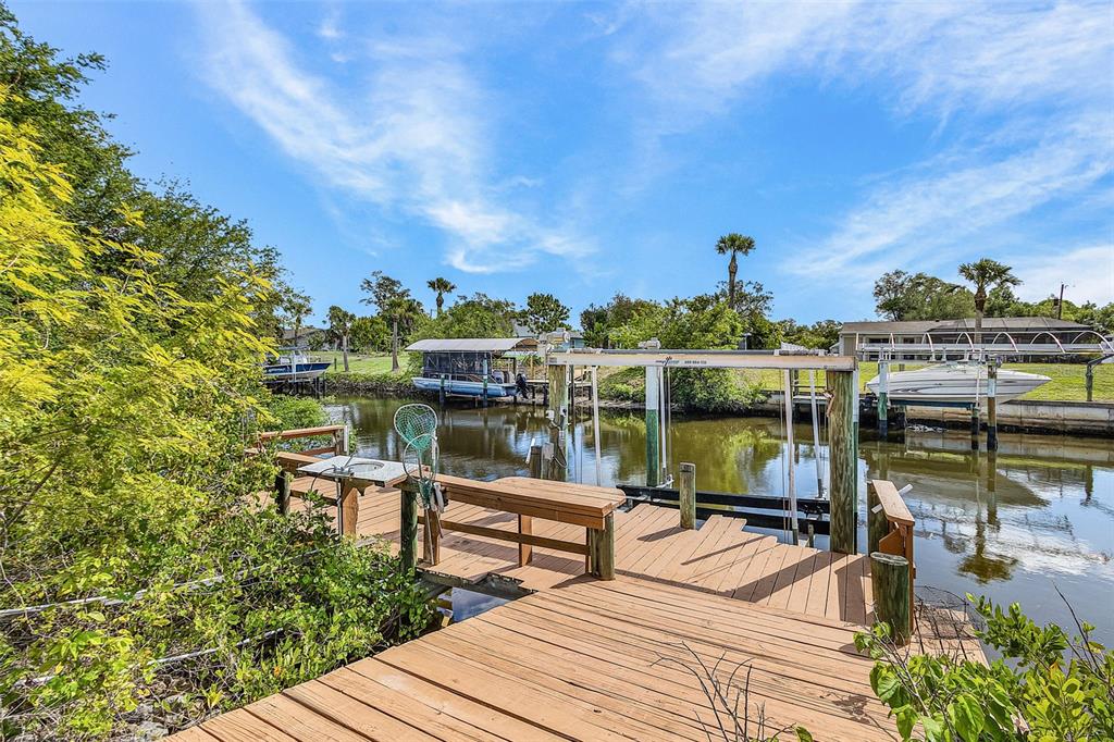 A wooden boat dock with a lift sits on a canal surrounded by lush greenery — 2368 PELLAM BOULEVARD, PORT CHARLOTTE, FL