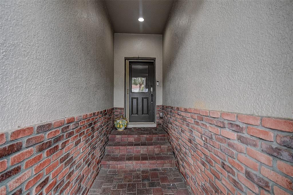 A recessed entryway features brick steps, brick lower walls, and a dark front door — 1426 HILLVIEW LANE, TARPON SPRINGS, FL