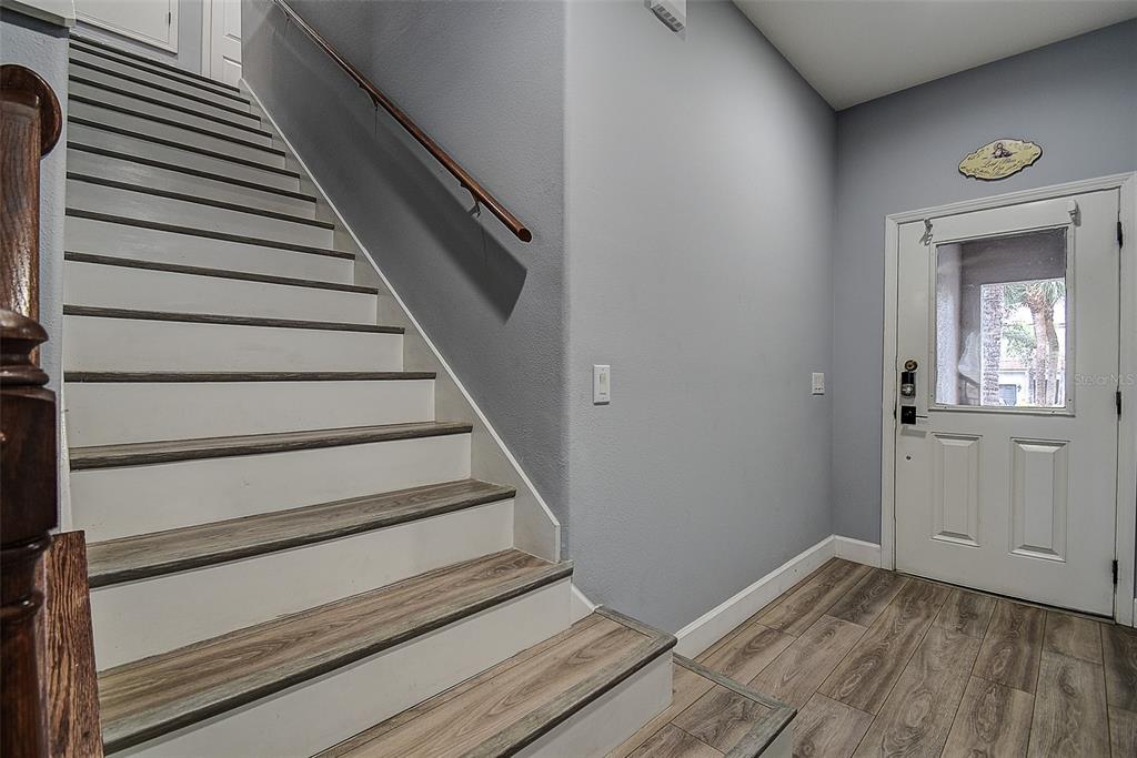 A staircase with wood-look treads and white risers sits beside a white front door — 1426 HILLVIEW LANE, TARPON SPRINGS, FL