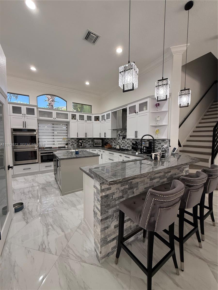 A modern kitchen features white cabinetry, gray stone countertops, a breakfast bar, and marble flooring — 18610 SW 39th Ct, Miramar FL 33029, MIRAMAR, FL