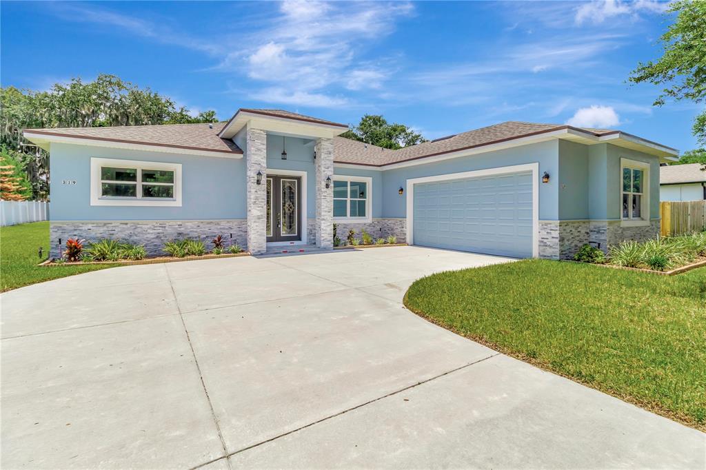 A light blue single-story house features a stone-accented entryway and a two-car garage — 319 WATER SHORE DRIVE, LEESBURG, FL