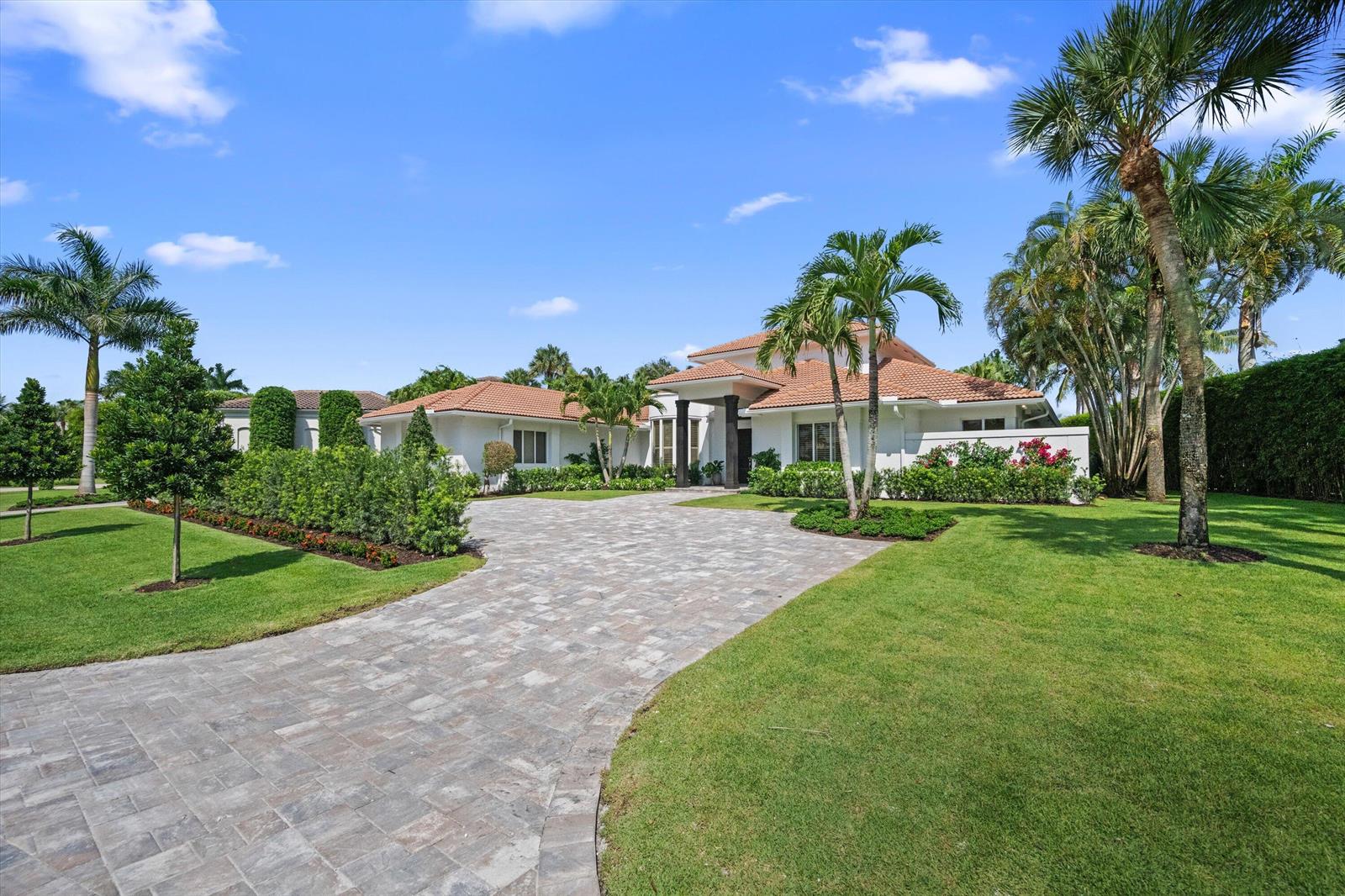 A white house with a tile roof and a paved driveway sits on a grassy lawn — 2432 Golf Brook Drive, Wellington FL 33414, WELLINGTON, FL