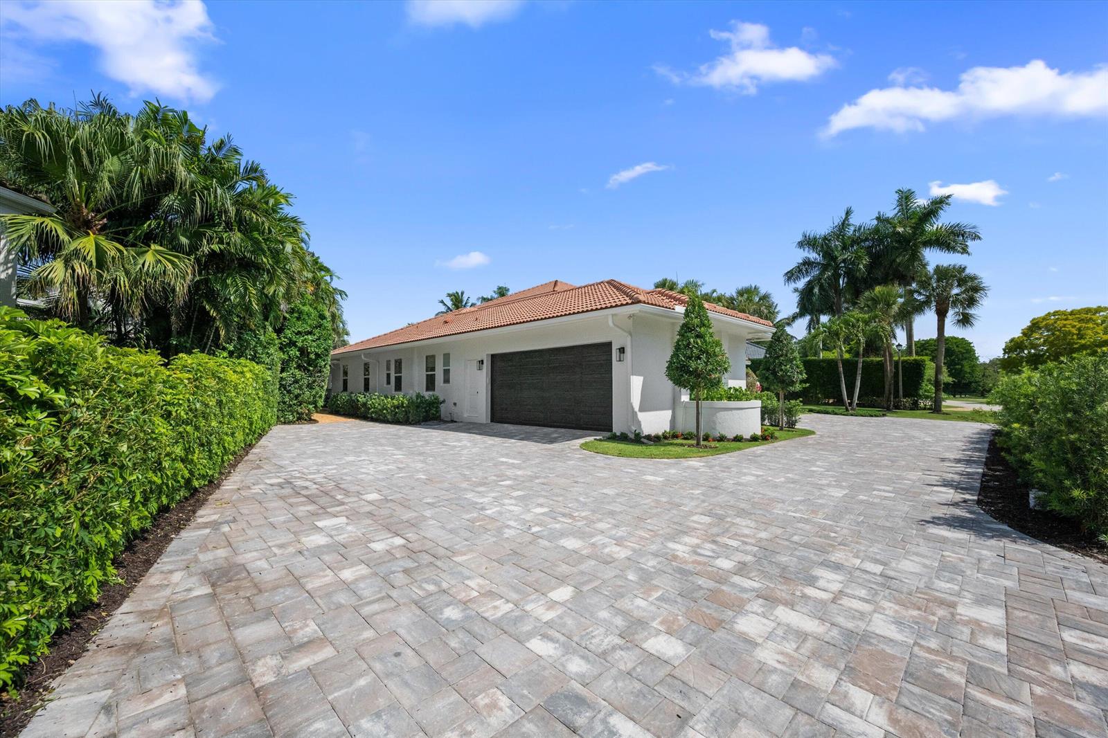 A white house with a tile roof and a dark garage door sits behind a paver driveway — 2432 Golf Brook Drive, Wellington FL 33414, WELLINGTON, FL
