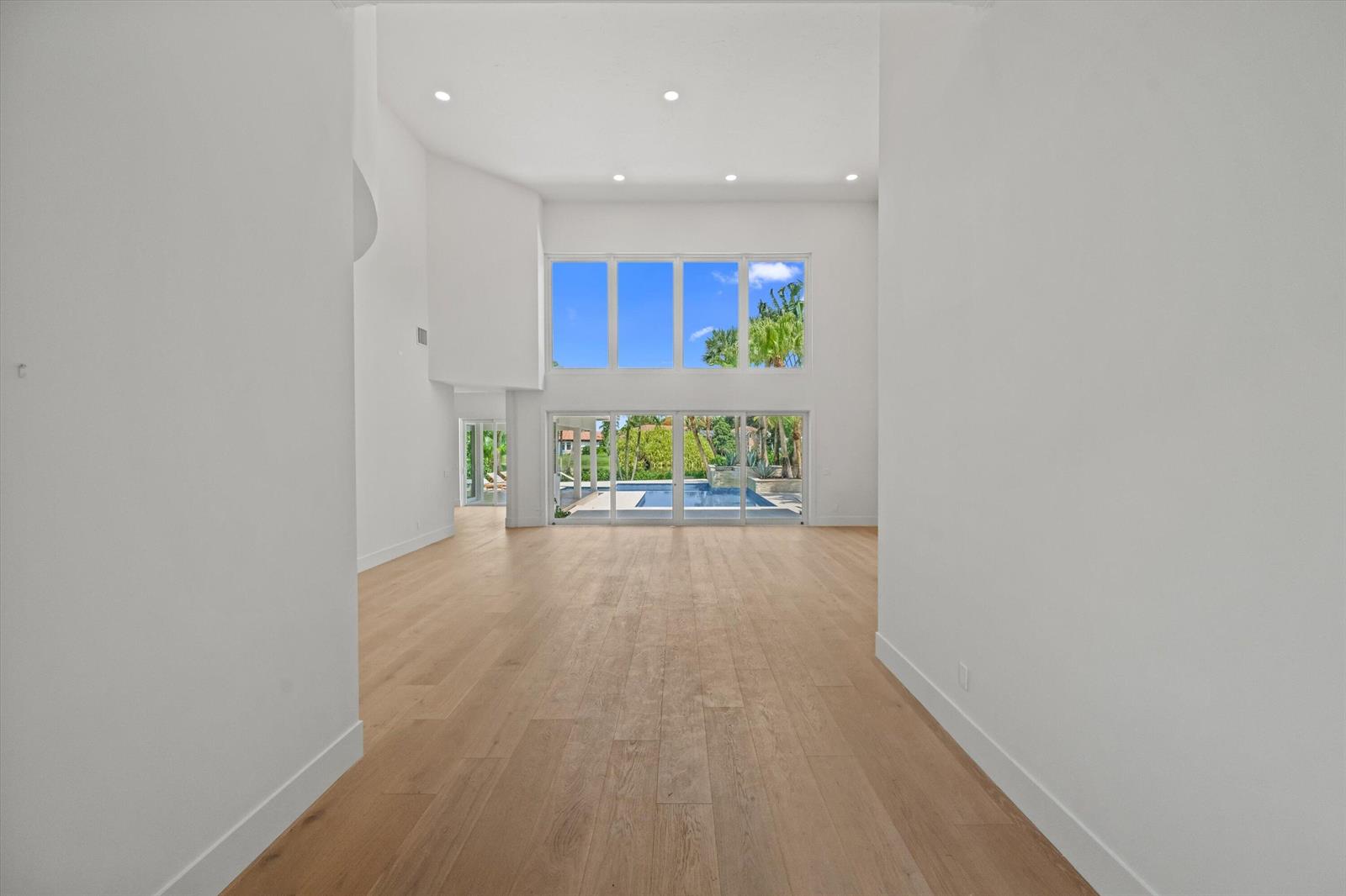 A spacious, empty living room features high ceilings, light wood flooring, and large glass doors — 2432 Golf Brook Drive, Wellington FL 33414, WELLINGTON, FL