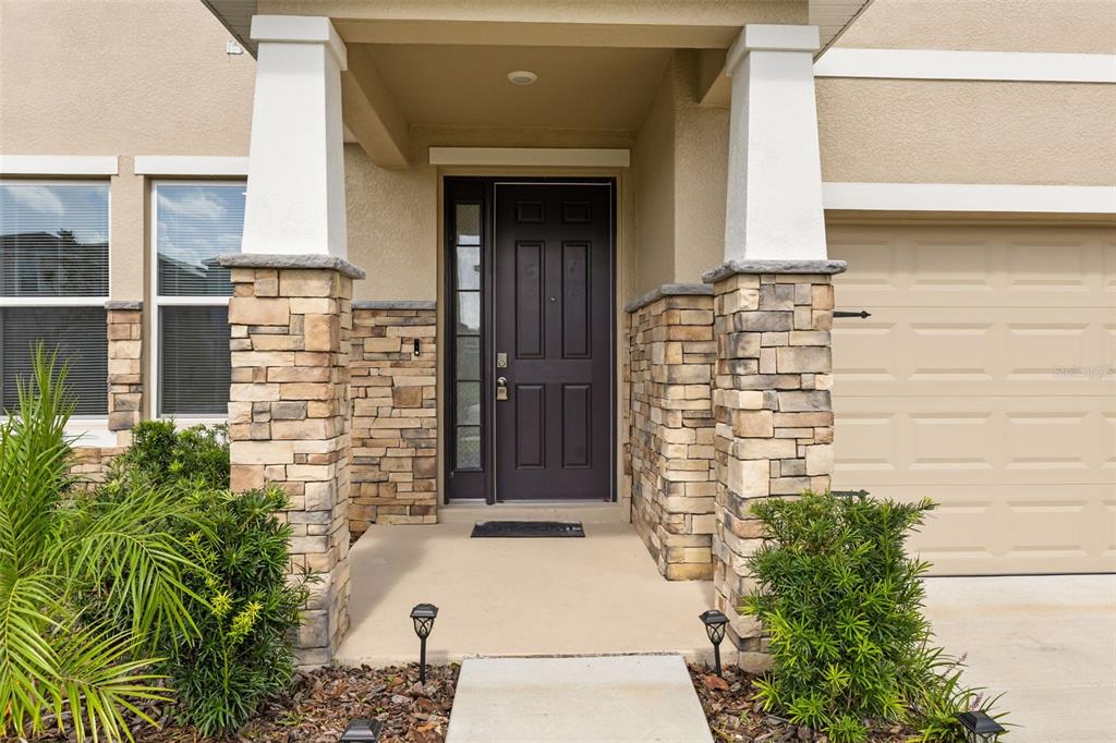The exterior of a house features a dark front door, stone columns, and a garage — 6764 BROAD RIVER AVENUE, LAND O LAKES, FL