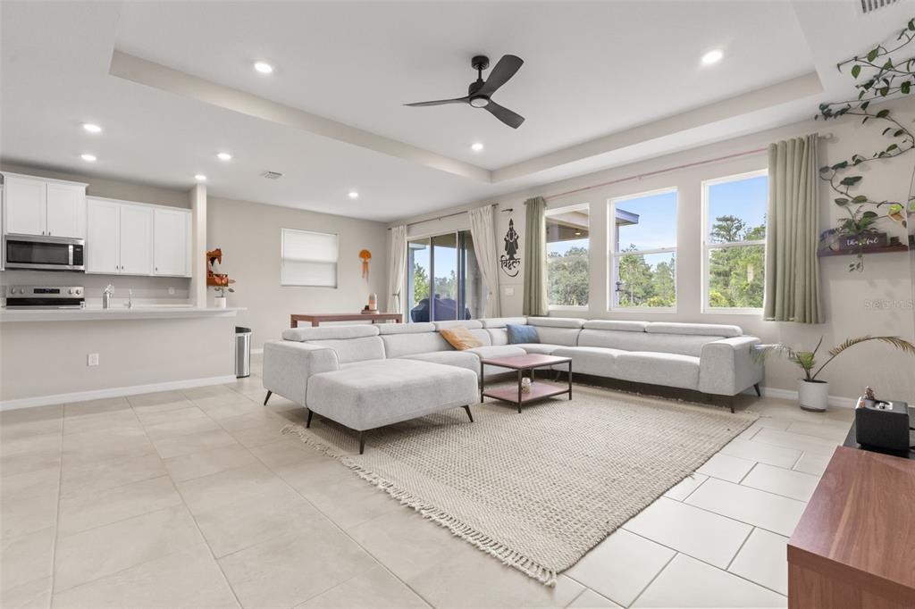 A spacious living room features light tile floors, a large sectional sofa, and recessed lighting — 6764 BROAD RIVER AVENUE, LAND O LAKES, FL