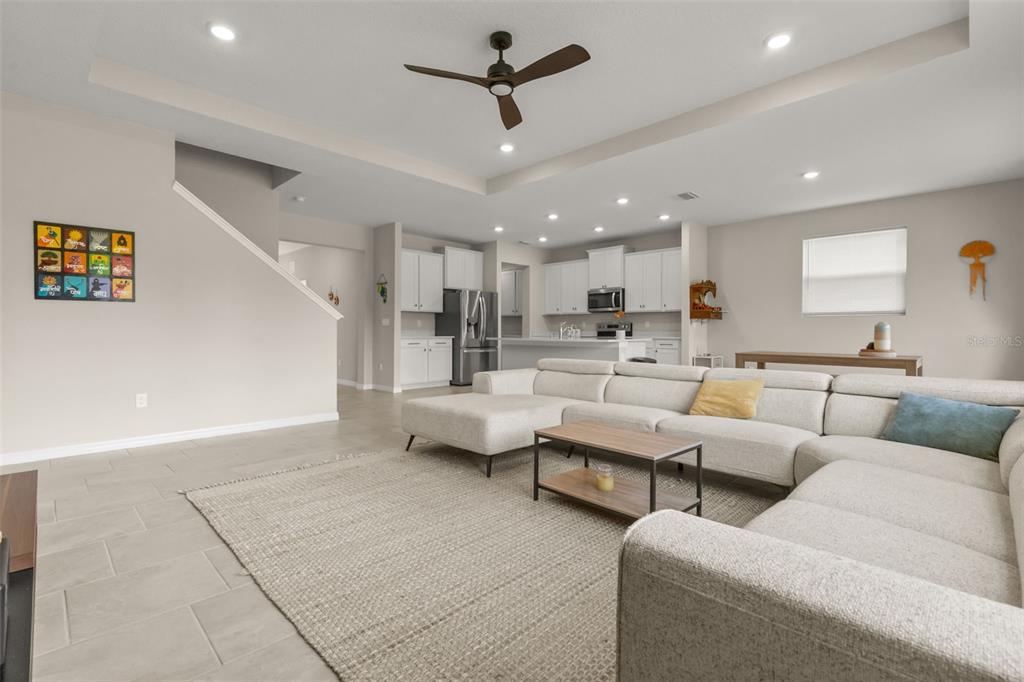 A spacious open-concept living room features a large sectional sofa, tile flooring, and a kitchen — 6764 BROAD RIVER AVENUE, LAND O LAKES, FL