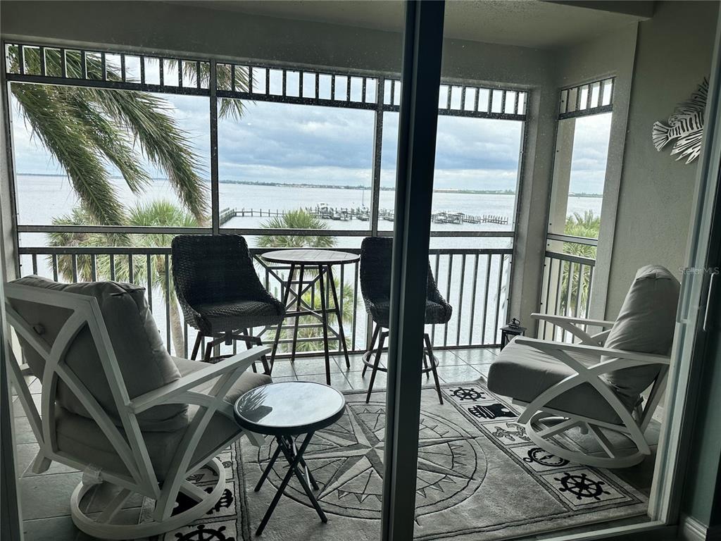 A screened-in balcony features outdoor furniture and a nautical-themed rug overlooking a waterfront view — 5114 MELBOURNE STREET UNIT A302, PUNTA GORDA, FL