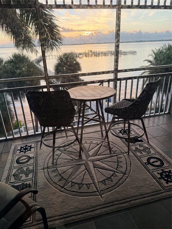A balcony with a small table and two chairs overlooks a sunset over the water — 5114 MELBOURNE STREET UNIT A302, PUNTA GORDA, FL