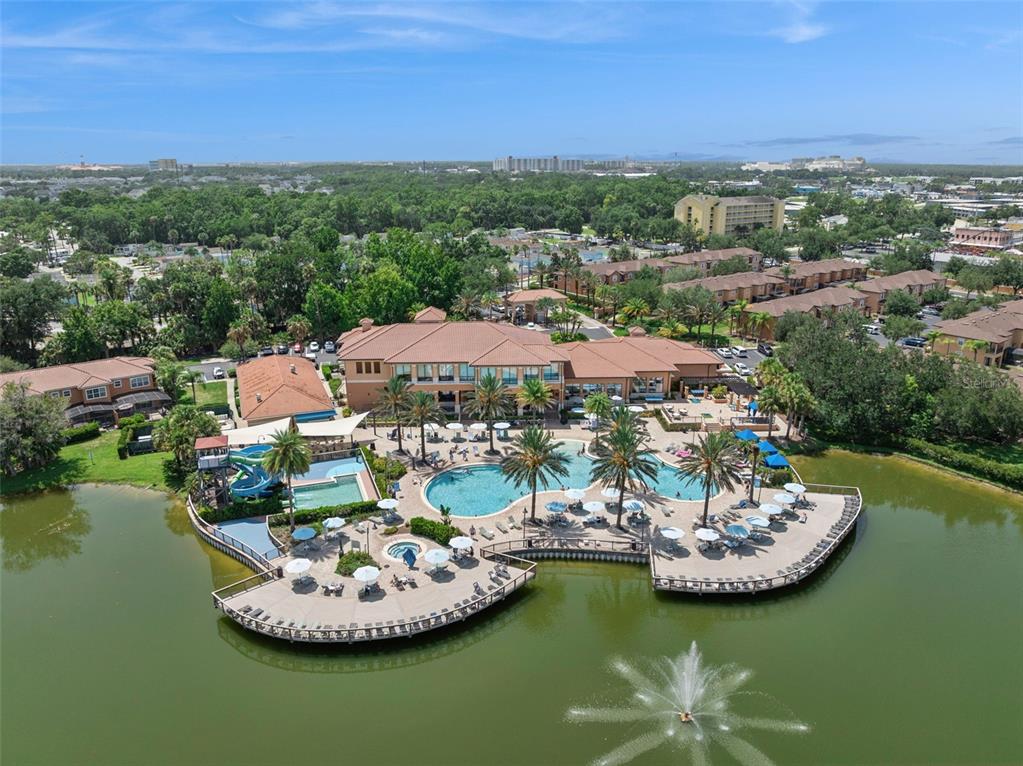 An aerial view shows a resort clubhouse with a pool, water slide, and lake fountain — 2717 BUSHMAN DR, KISSIMMEE, FL