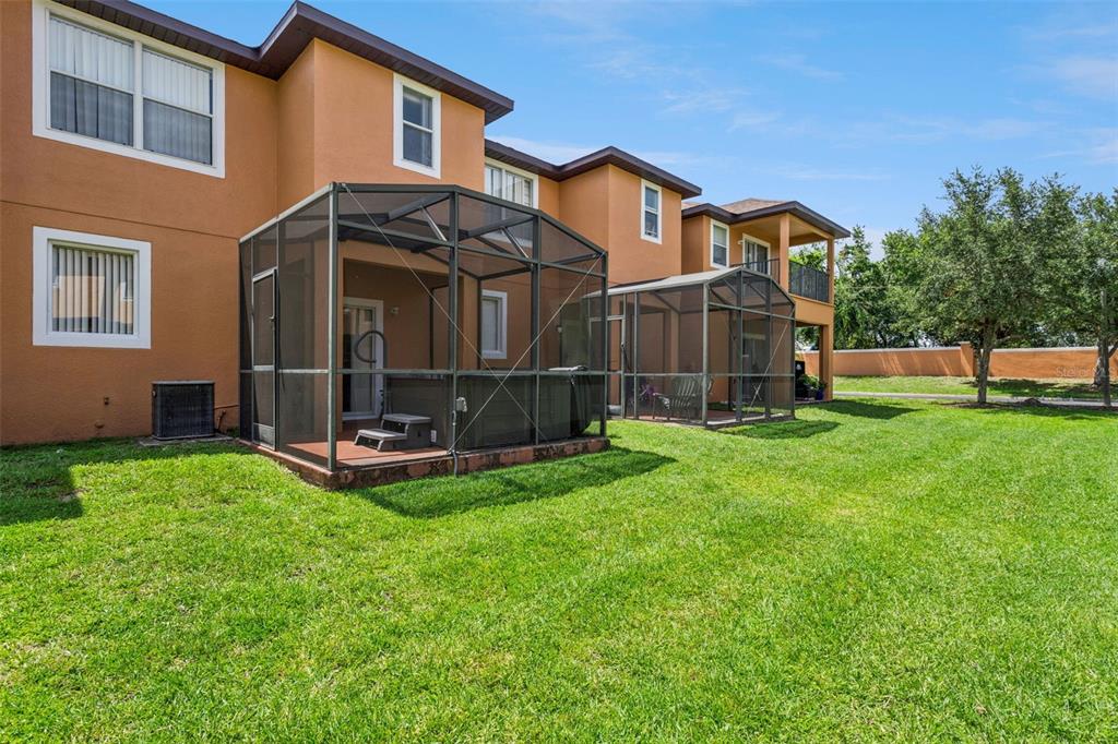 The rear exterior of a two-story tan townhouse features two screened-in lanais and a lawn — 2717 BUSHMAN DR, KISSIMMEE, FL