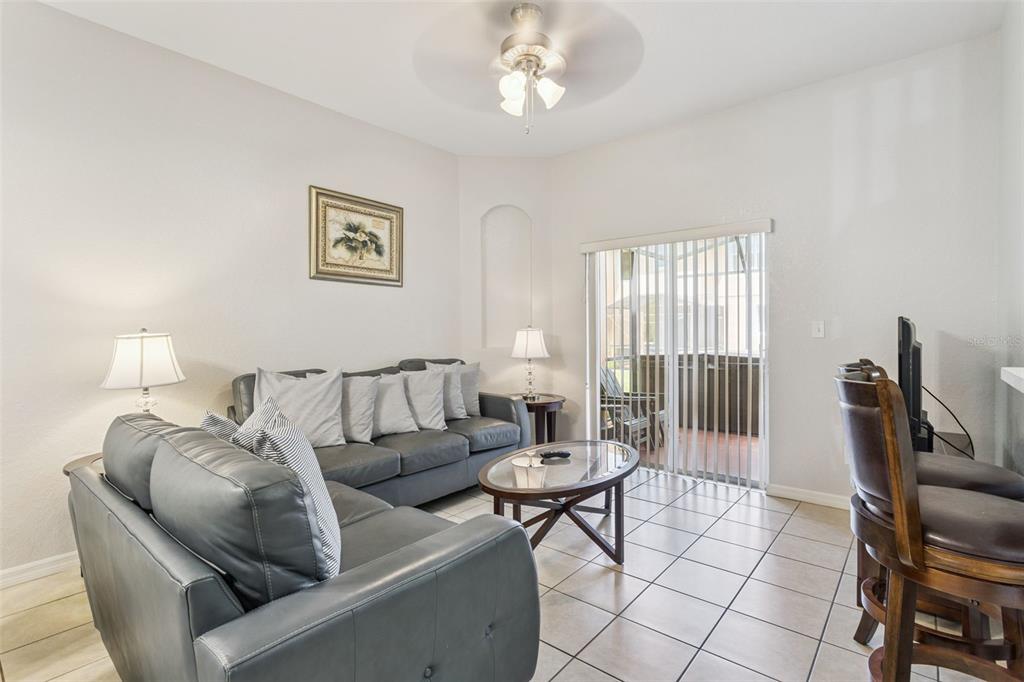 A living room with tile floors, a gray sofa, a glass coffee table, and sliding doors — 2717 BUSHMAN DR, KISSIMMEE, FL