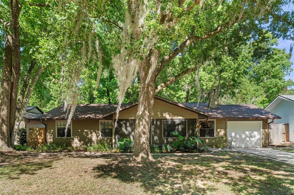 A single-story house with brown siding and a garage sits behind a large oak tree — 3724 NW 53RD TERRACE, GAINESVILLE, FL
