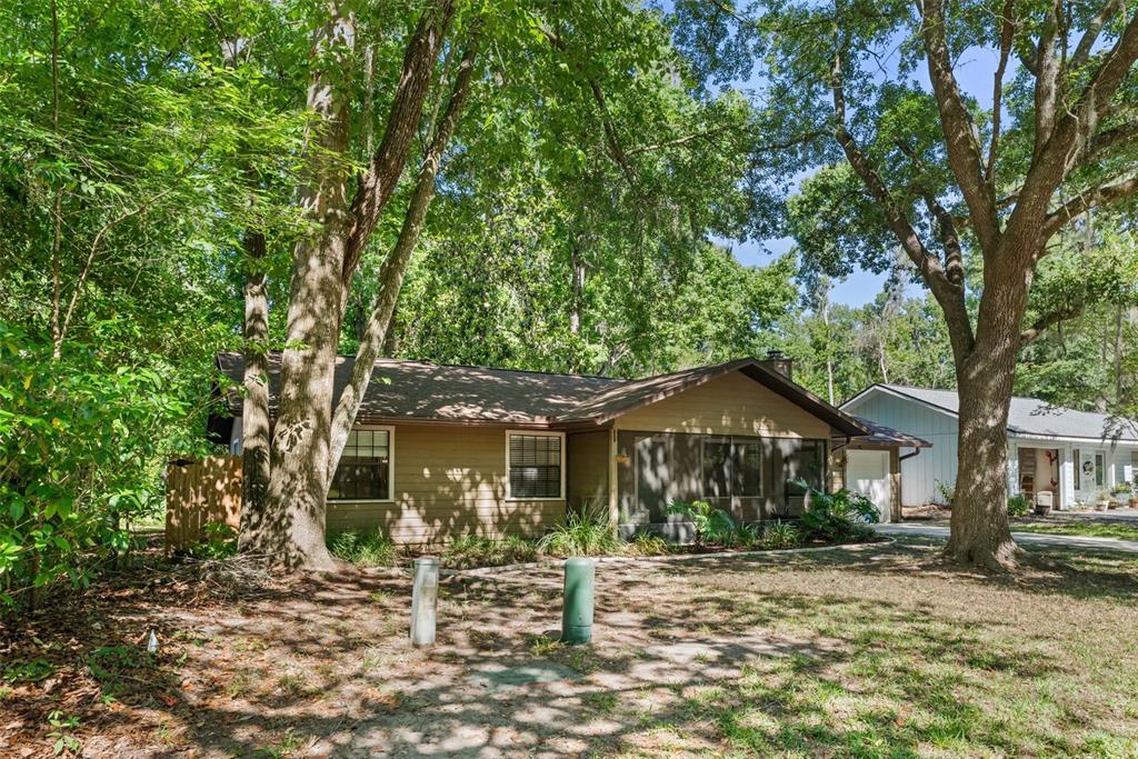 A single-story house with tan siding and a screened porch sits among many large trees — 3724 NW 53RD TERRACE, GAINESVILLE, FL