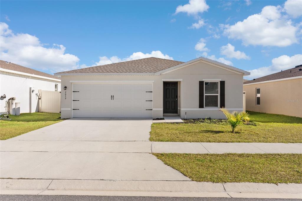 A single-story house with a white garage, dark front door, and a concrete driveway — 2059 KENTUCKY ROAD, SUMTERVILLE, FL