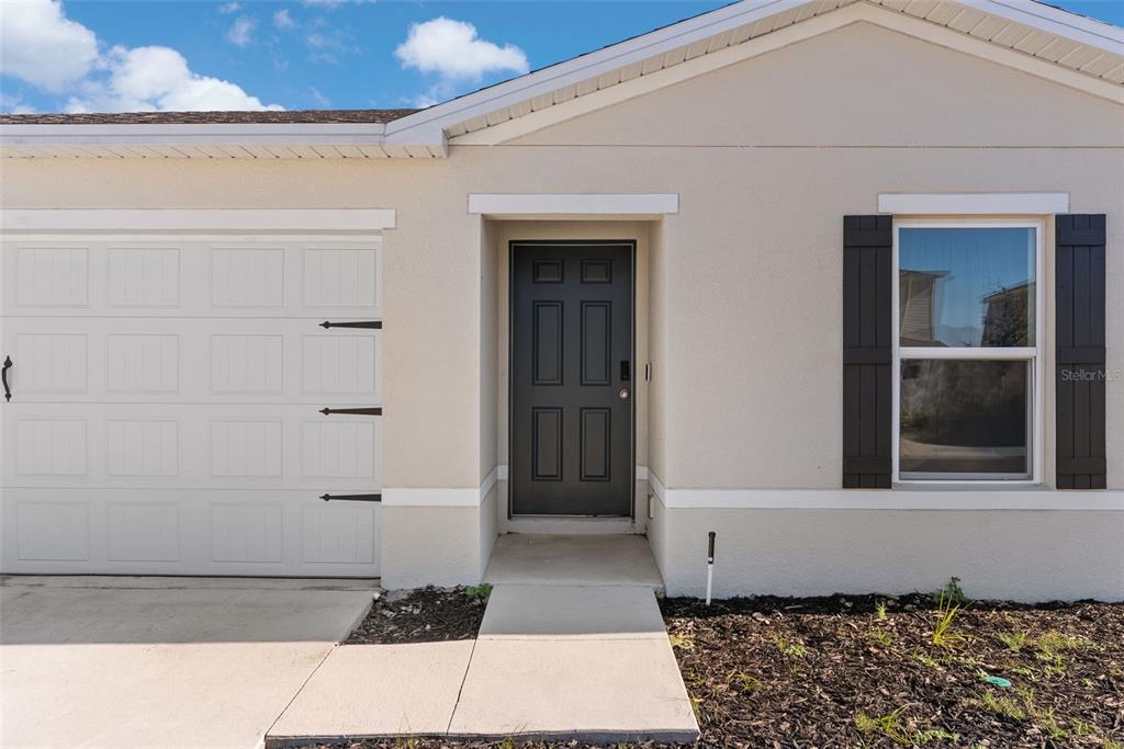 The exterior of a house features a white garage door, a dark front door, and shutters — 2059 KENTUCKY ROAD, SUMTERVILLE, FL