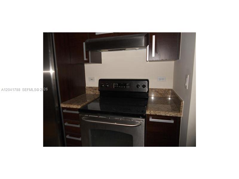 A kitchen features dark wood cabinets, granite countertops, and a stainless steel electric range — 2525 SW 3 AV # 1006, Miami FL 33129, MIAMI, FL