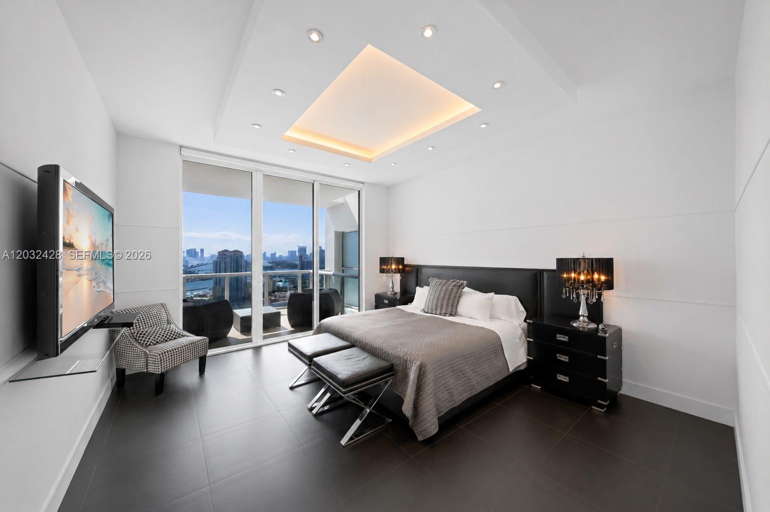 A modern bedroom features a king bed, dark tile floors, and floor-to-ceiling windows with city views — 50 S Pointe Dr # 3103, Miami Beach FL 33139, MIAMI BEACH, FL