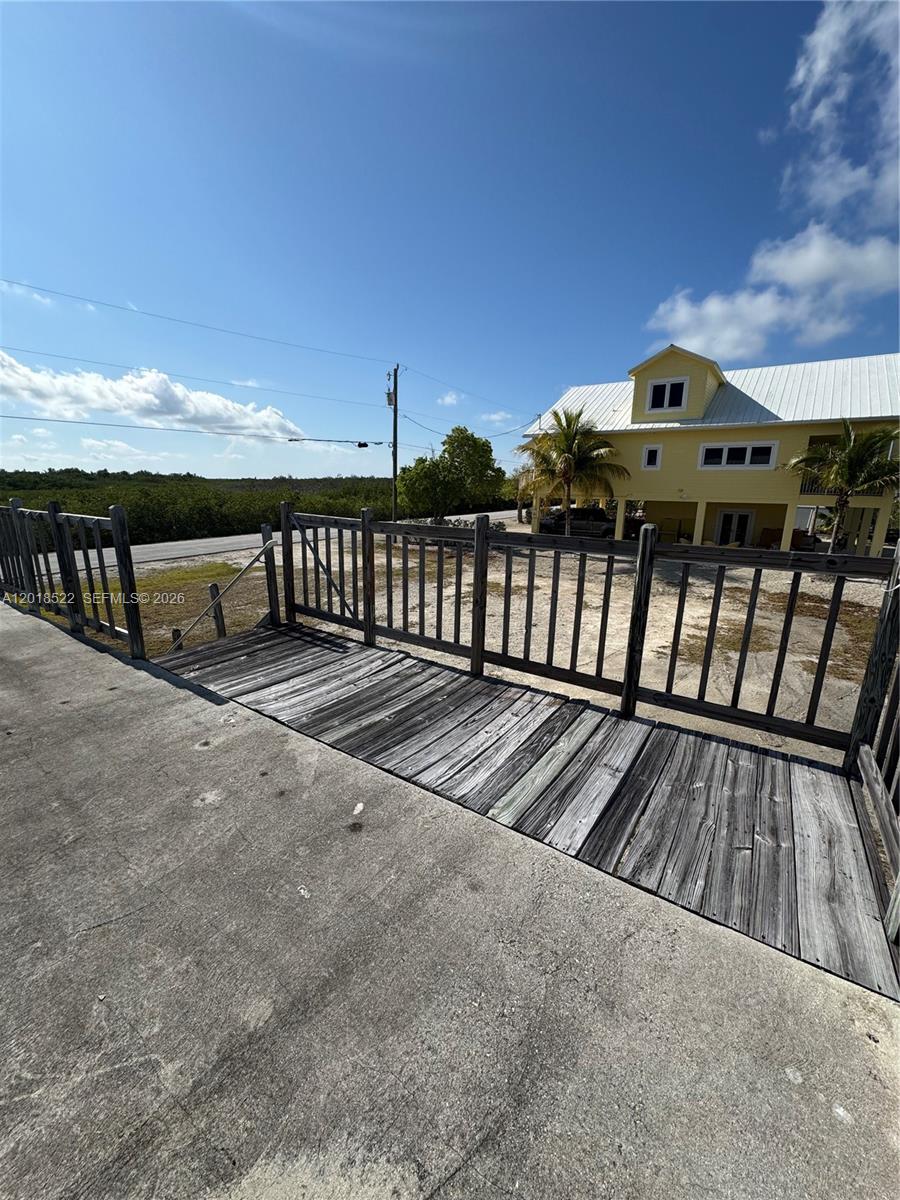 A wooden deck with a railing overlooks a sandy lot and a yellow house — 4276 Dorn Road, Torch Key FL 33042, TORCH KEY, FL