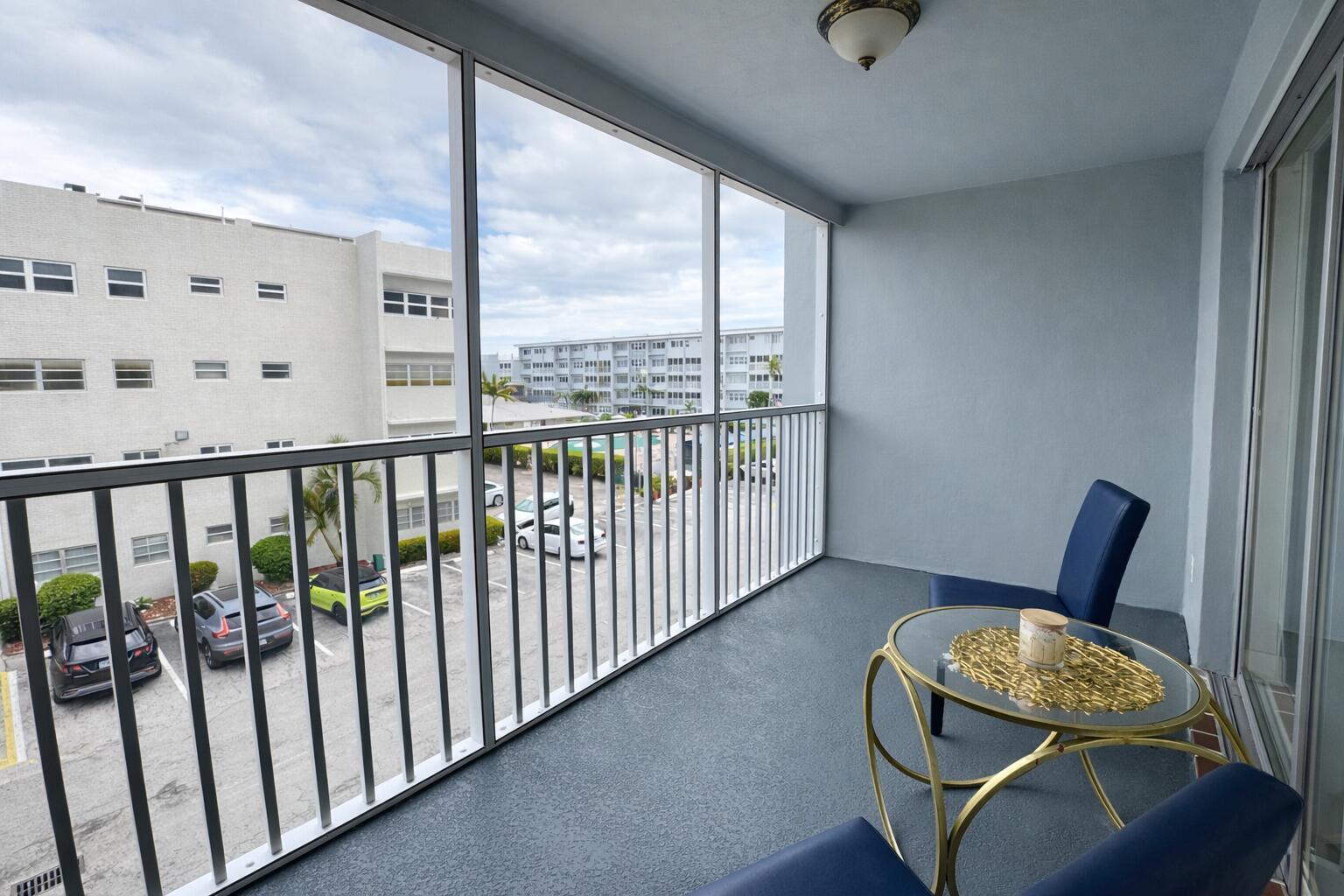 A screened-in balcony with blue chairs, a glass-topped table, and a view of a parking lot — 215 SE 3RD Avenue # 306D, Hallandale Beach FL 33009, HALLANDALE BEACH, FL