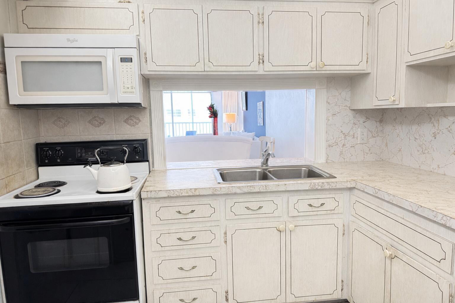 A kitchen features white cabinets, a black stove, a stainless steel sink, and laminate countertops — 215 SE 3RD Avenue # 306D, Hallandale Beach FL 33009, HALLANDALE BEACH, FL