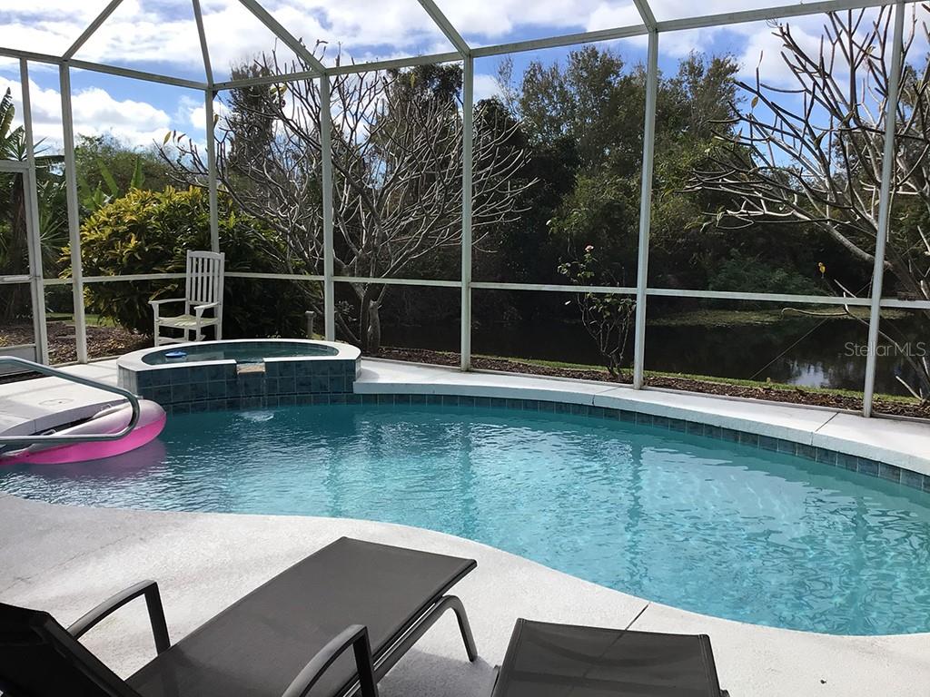A screened-in pool and hot tub overlook a pond with trees in the background — 6222 BUCKINGHAM STREET, SARASOTA, FL