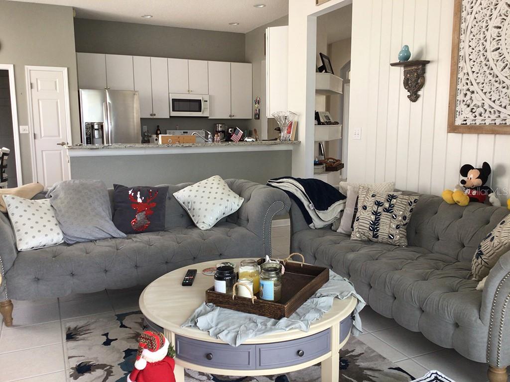 A living room with two grey tufted sofas faces a kitchen with white cabinets — 6222 BUCKINGHAM STREET, SARASOTA, FL