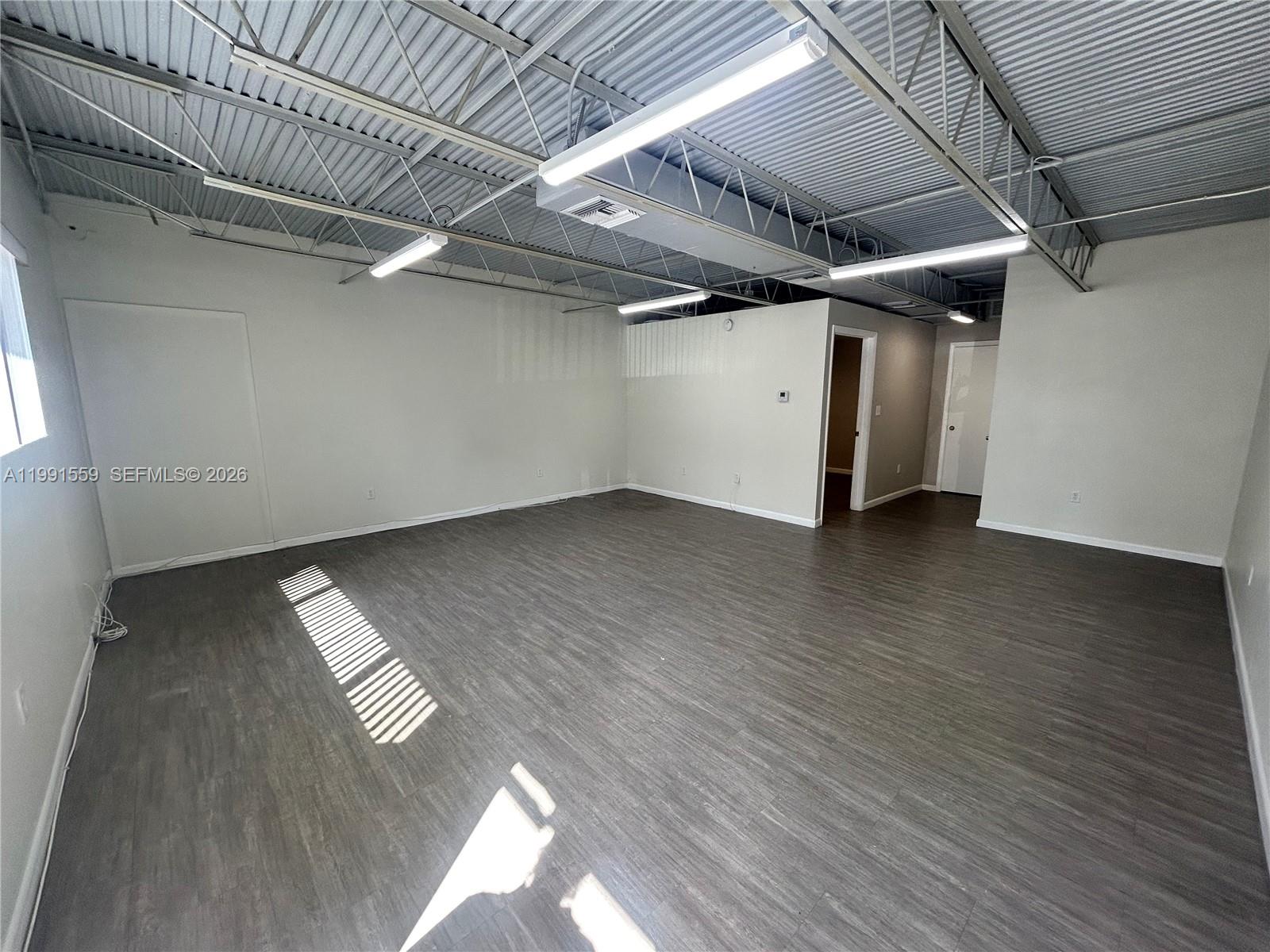 An empty office space features gray wood-look flooring, light-colored walls, and an exposed metal ceiling — 6225 Johnson St, Hollywood FL 33024, HOLLYWOOD, FL