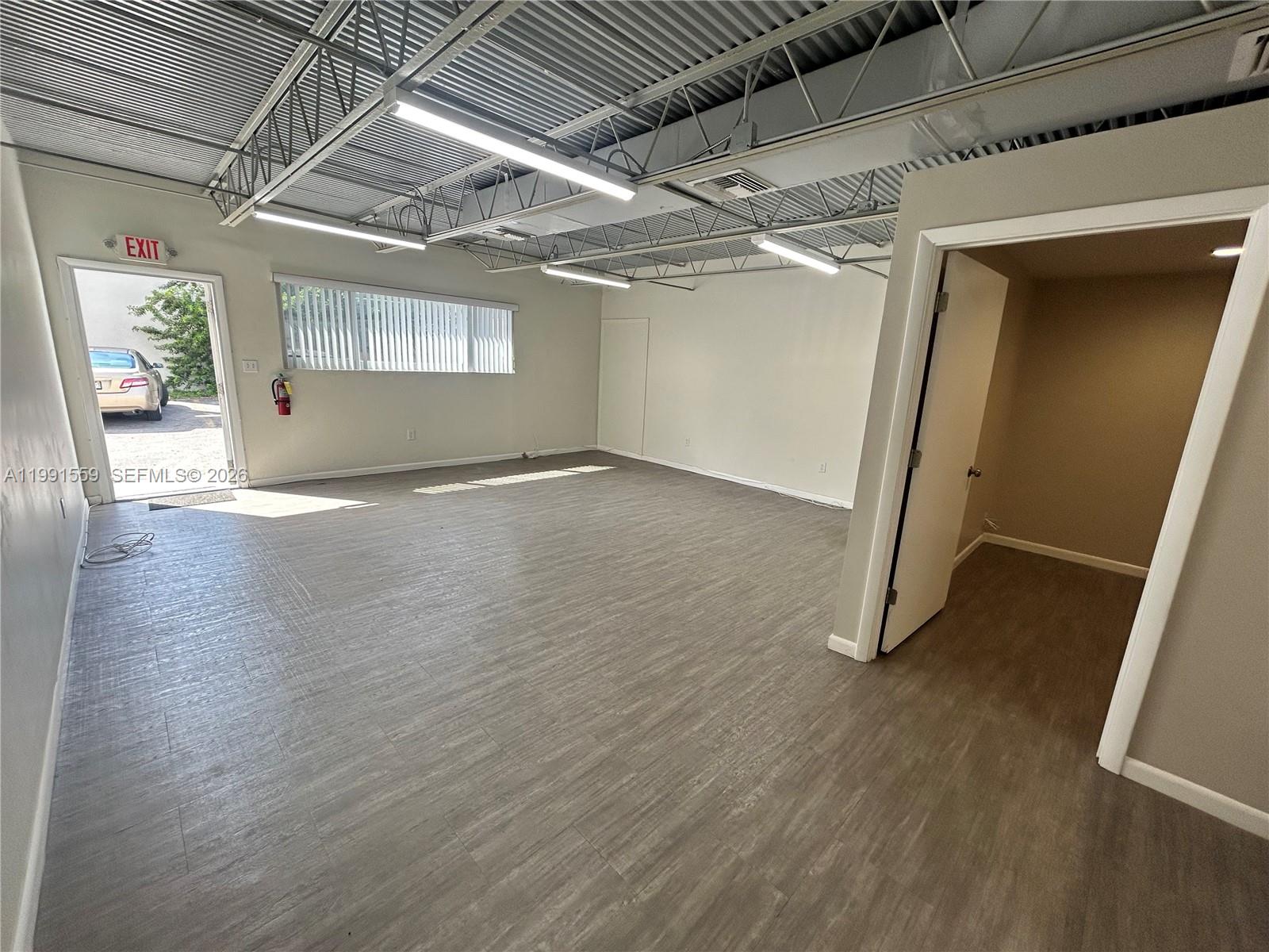 An empty office space features gray wood-look flooring, exposed ceiling trusses, and an open doorway — 6225 Johnson St, Hollywood FL 33024, HOLLYWOOD, FL