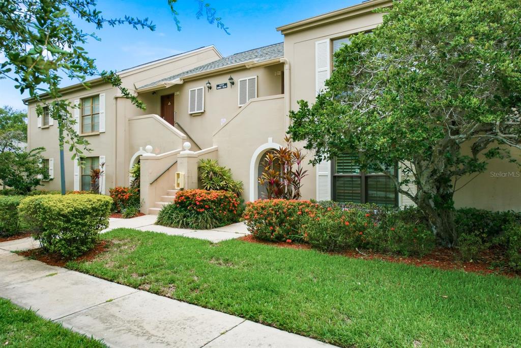 A two-story tan apartment building with stairs leading to an upper-level entrance — 2453 EGRET BOULEVARD UNIT O102, CLEARWATER, FL