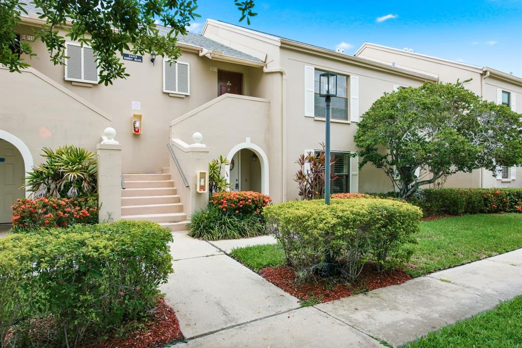 A two-story tan apartment building features an exterior staircase, landscaping, and a sidewalk — 2453 EGRET BOULEVARD UNIT O102, CLEARWATER, FL
