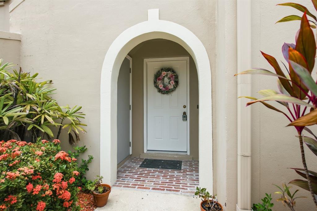 A white front door with a floral wreath sits inside a beige arched entryway — 2453 EGRET BOULEVARD UNIT O102, CLEARWATER, FL