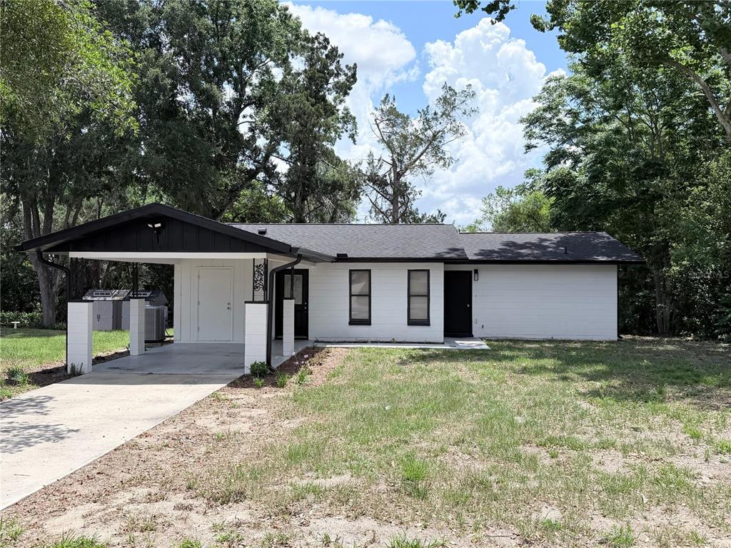 A single-story house with white siding, a black roof, and an attached carport — 11 BAHIA COURT LOOP, OCALA, FL