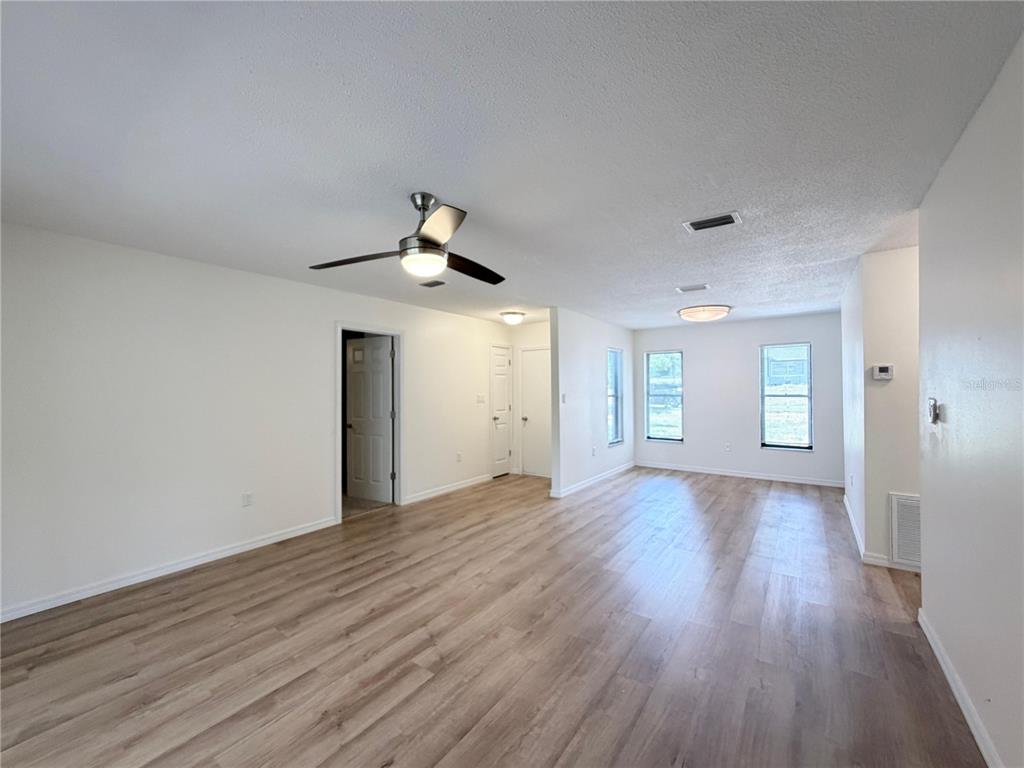 An empty living room features light wood-look flooring, white walls, a ceiling fan, and windows — 11 BAHIA COURT LOOP, OCALA, FL