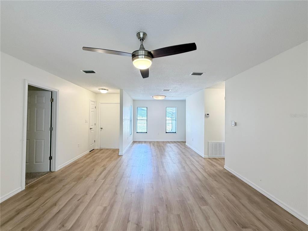 A bright, empty room features light wood-look flooring, white walls, and a ceiling fan — 11 BAHIA COURT LOOP, OCALA, FL
