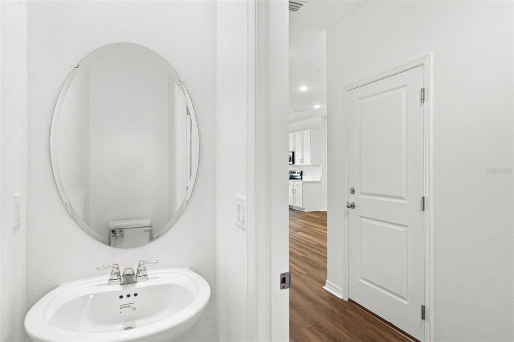 A white bathroom vanity with an oval mirror sits beside a doorway leading to a kitchen — 4899 WINDING RIVER ROAD, ORLANDO, FL