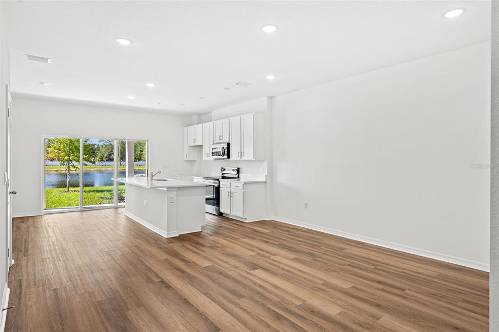 An open-concept kitchen and living area features white cabinets, an island, and wood-look flooring — 4899 WINDING RIVER ROAD, ORLANDO, FL