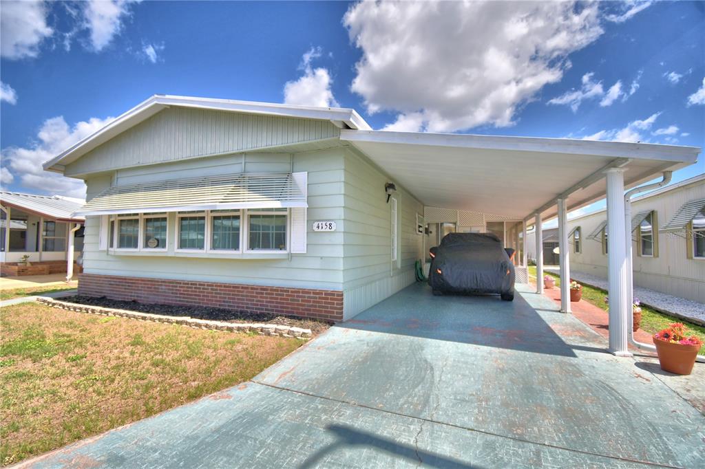 A light green manufactured home features a brick base, a carport, and a covered driveway — 4158 ROLLING OAKS DRIVE, WINTER HAVEN, FL