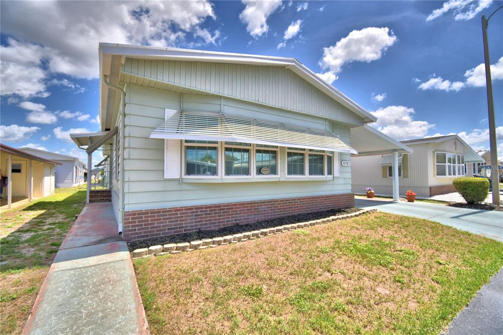A light green manufactured home with a brick base, metal awning, and attached carport — 4158 ROLLING OAKS DRIVE, WINTER HAVEN, FL
