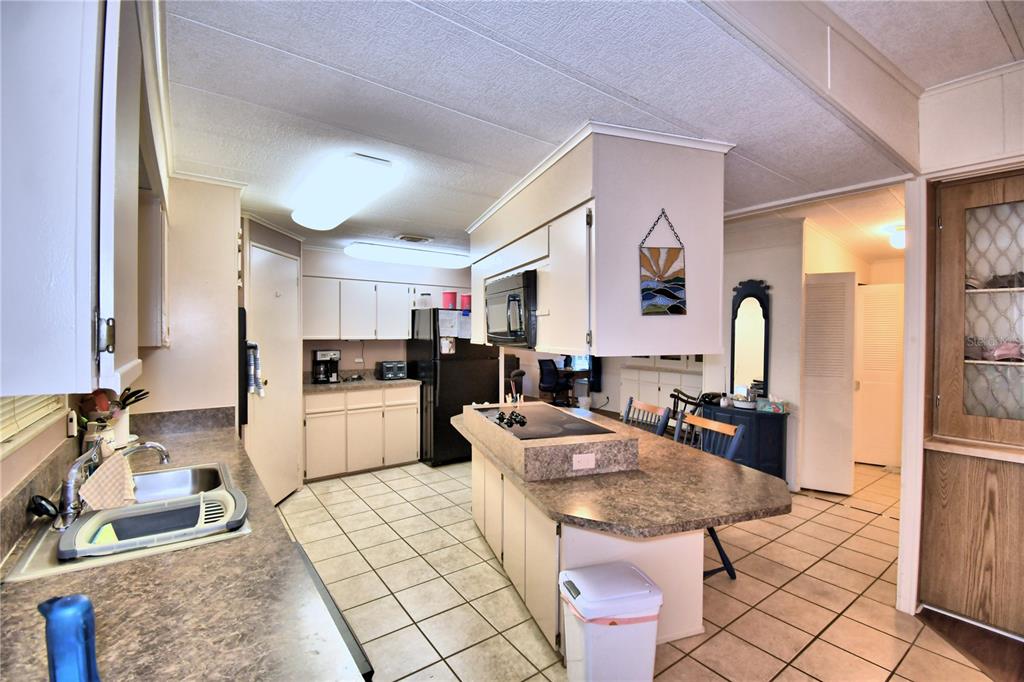A kitchen features light-colored cabinets, a central island with a cooktop, and tiled flooring — 4158 ROLLING OAKS DRIVE, WINTER HAVEN, FL
