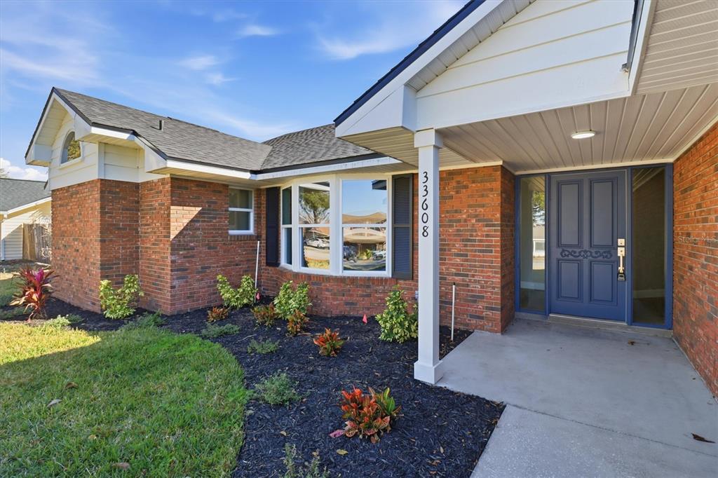 A brick house exterior features a blue front door and a bay window at dusk — 33608 OVERTON DRIVE, LEESBURG, FL