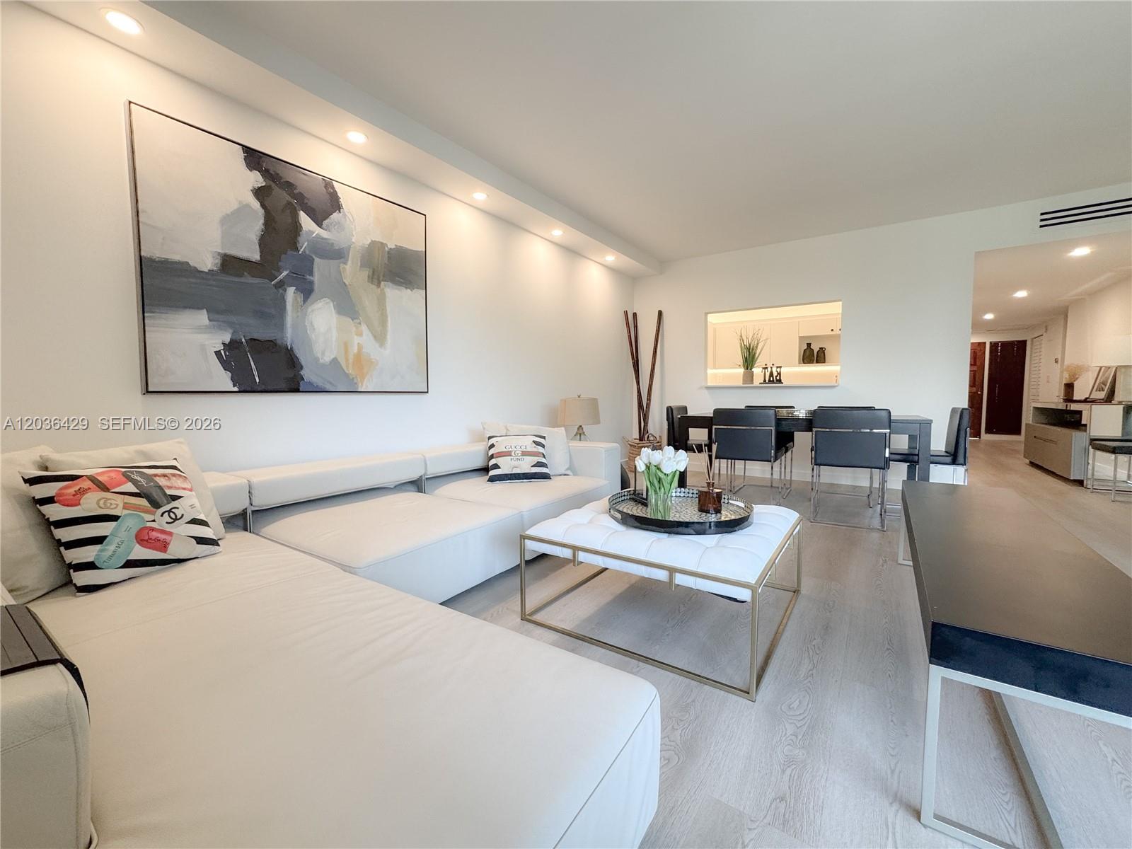 A modern living room features a white sectional sofa, a tufted coffee table, and artwork — 101 Crandon Blvd # 170, Key Biscayne FL 33149, KEY BISCAYNE, FL