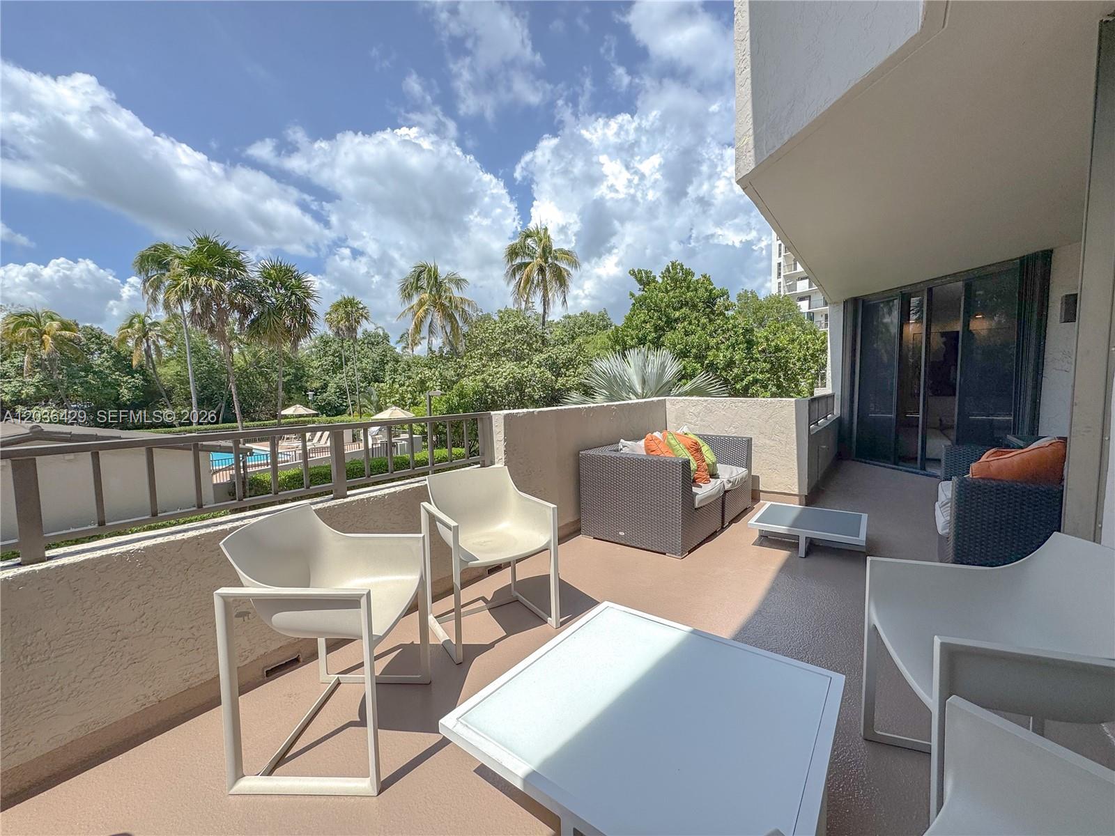 A balcony features white modern chairs, a small table, and wicker seating overlooking palm trees — 101 Crandon Blvd # 170, Key Biscayne FL 33149, KEY BISCAYNE, FL