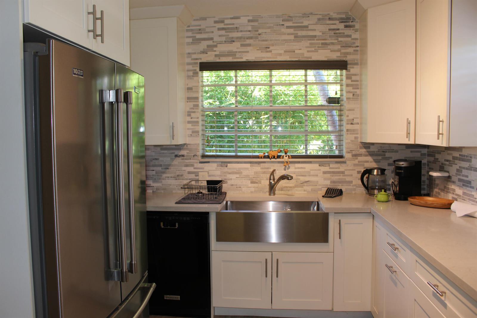 A kitchen features white cabinets, a stainless steel farmhouse sink, and a mosaic tile backsplash — 225 Gulfstream Boulevard, Boynton Beach FL 33435, BOYNTON BEACH, FL