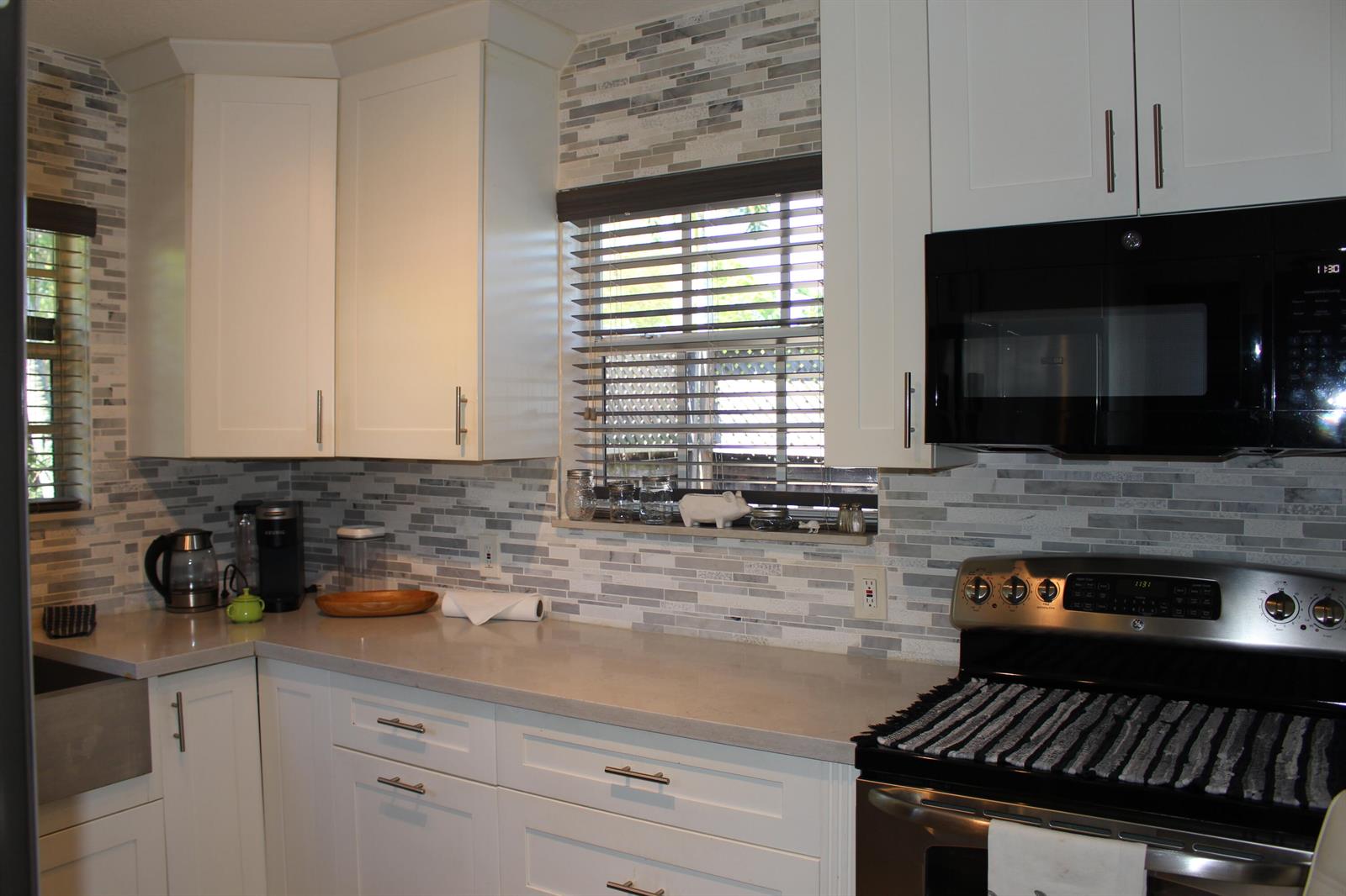A kitchen features white cabinets, a gray tiled backsplash, stainless steel appliances, and quartz countertops — 225 Gulfstream Boulevard, Boynton Beach FL 33435, BOYNTON BEACH, FL