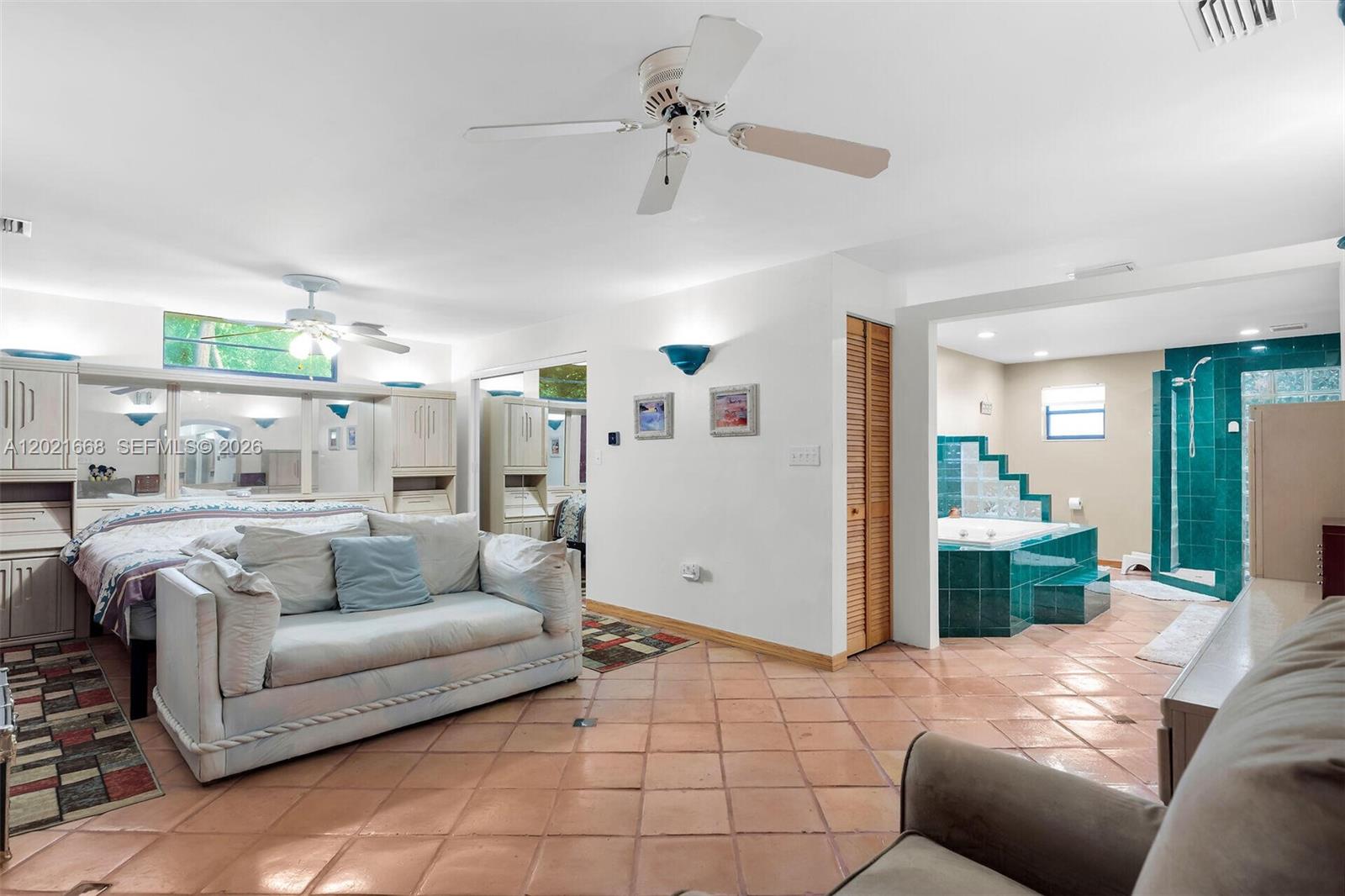 A bedroom with a sofa, bed, and an open-concept bathroom featuring teal tile accents — 323 Bay View Ave, Key Largo FL 33037, KEY LARGO, FL