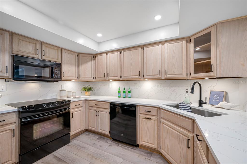 A kitchen features light wood cabinets, white marble-look countertops, and black appliances — 17920 GULF BOULEVARD UNIT 2008, REDINGTON SHORES, FL