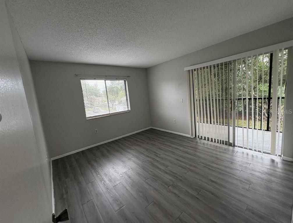 An empty room with gray wood-look flooring, a window with blinds, and a sliding glass door — 2683 OAK PARK WAY UNIT 214, ORLANDO, FL